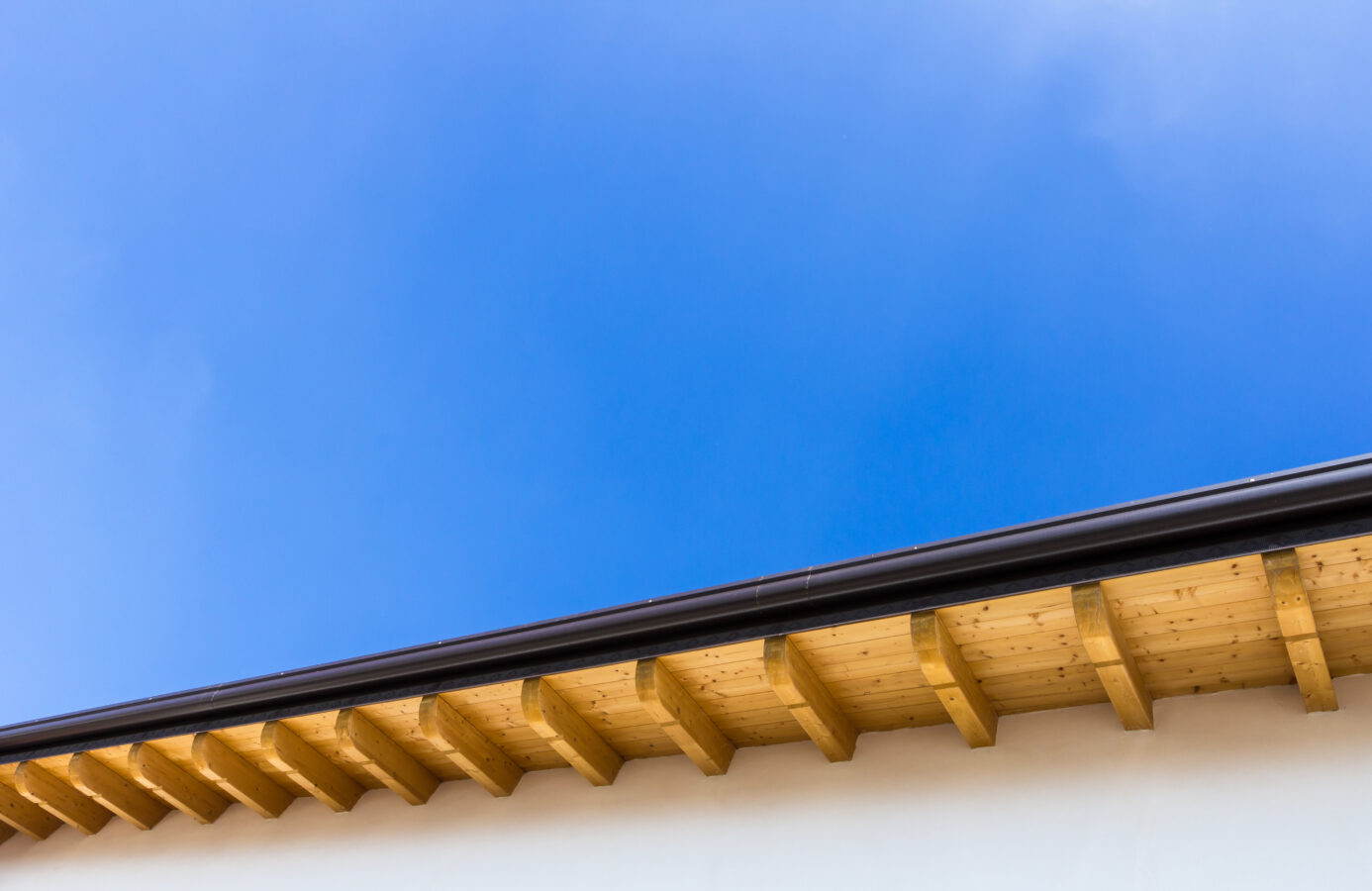 Low angle view of new house with wooden roof and gutter against clear blue sky